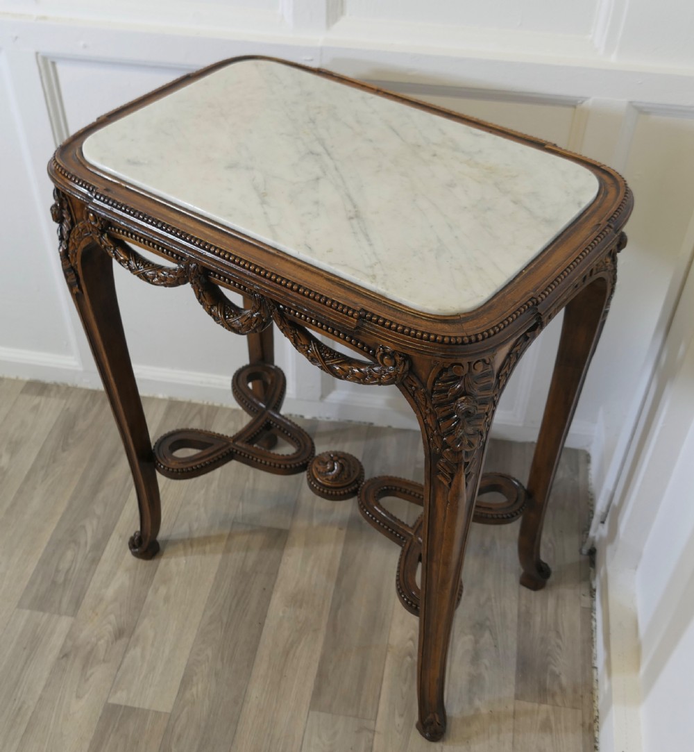A French carved wooden lamp table featuring a white marble top, sculpted floral garlands, and slender curved legs connected by an ornate stretcher. View XI