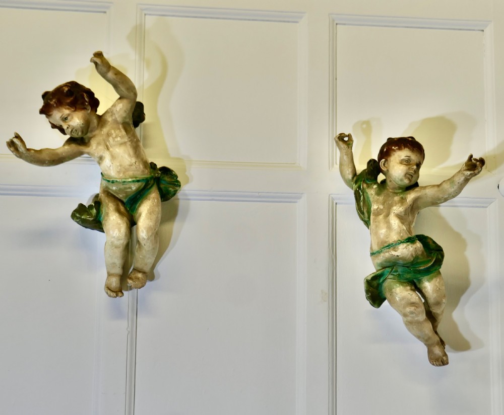 A pair of 19th-century Italian carved wood putti featuring painted dynamic poses and green drapery.
