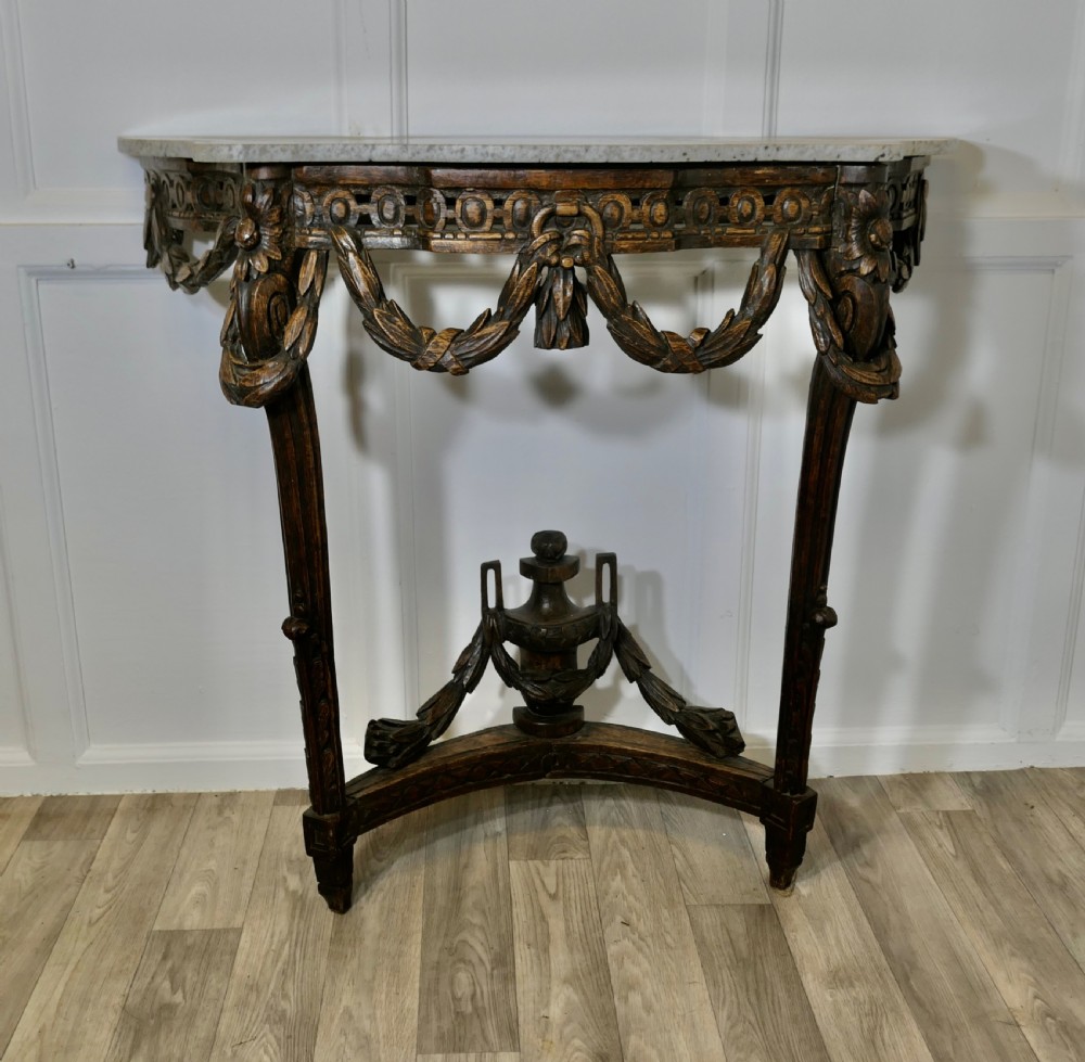A dark hand-carved wooden French Neoclassical console table featuring drape festoons, a guilloche apron, a curved stretcher with an urn finial, and a light granite top.