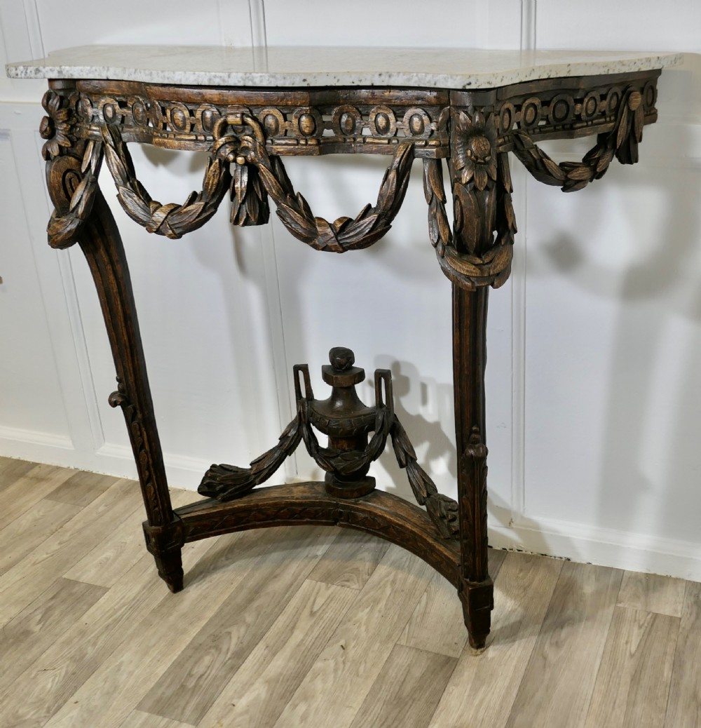 A dark hand-carved wooden French Neoclassical console table featuring drape festoons, a guilloche apron, a curved stretcher with an urn finial, and a light granite top. View II
