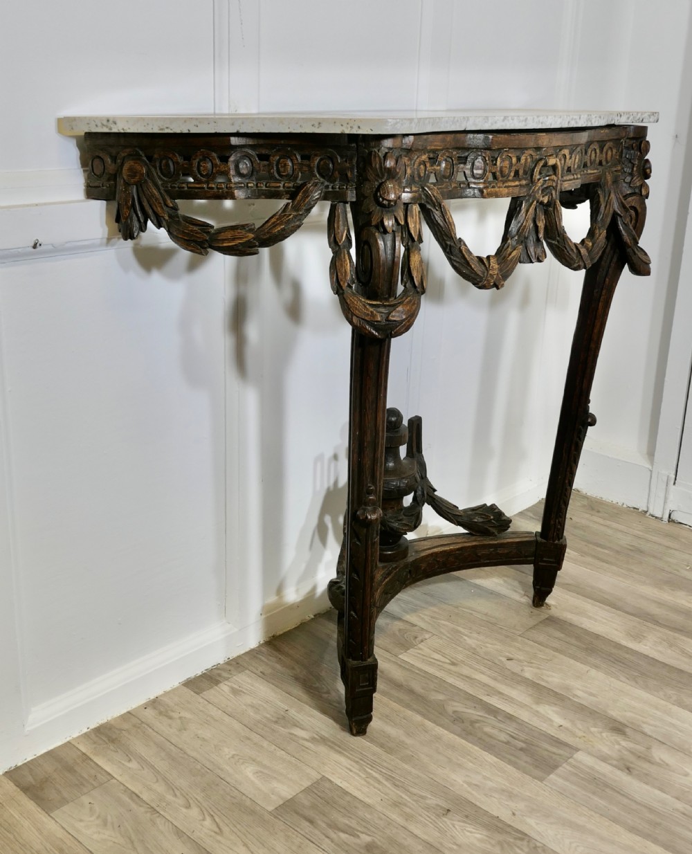 A dark hand-carved wooden French Neoclassical console table featuring drape festoons, a guilloche apron, a curved stretcher with an urn finial, and a light granite top. View V
