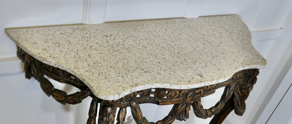 A dark hand-carved wooden French Neoclassical console table featuring drape festoons, a guilloche apron, a curved stretcher with an urn finial, and a light granite top. View VI