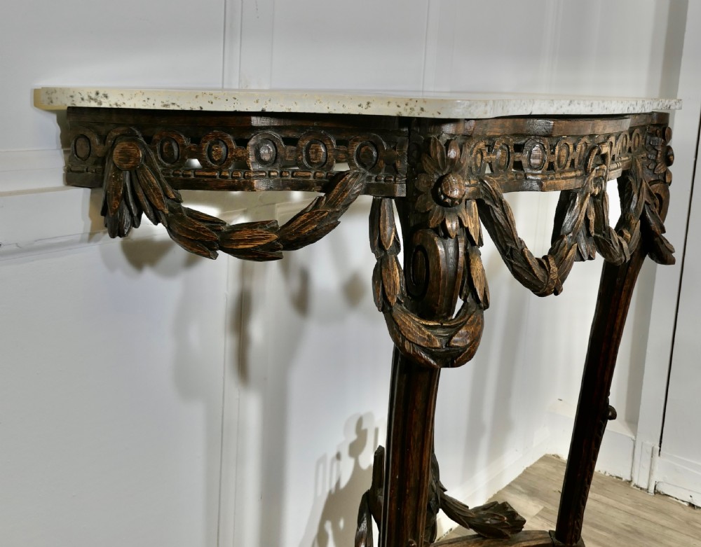 A dark hand-carved wooden French Neoclassical console table featuring drape festoons, a guilloche apron, a curved stretcher with an urn finial, and a light granite top. View VII