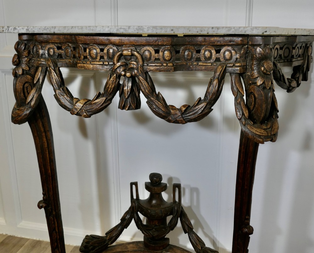 A dark hand-carved wooden French Neoclassical console table featuring drape festoons, a guilloche apron, a curved stretcher with an urn finial, and a light granite top. View VIII