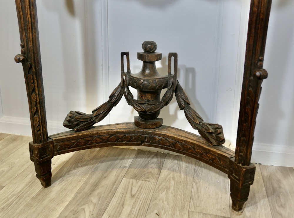 A dark hand-carved wooden French Neoclassical console table featuring drape festoons, a guilloche apron, a curved stretcher with an urn finial, and a light granite top. View IX