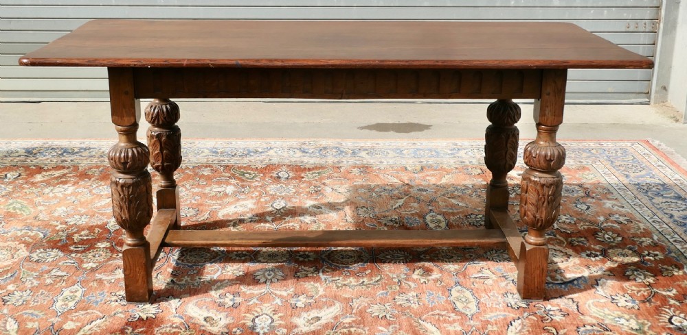 A rectangular solid oak refectory dining table featuring carved bulbous turned legs joined by a low central stretcher. View VII