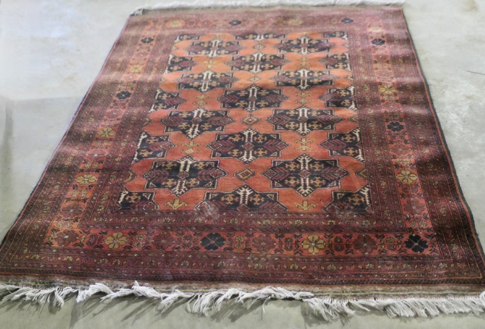 A rectangular vintage wool area rug featuring dark brown and navy geometric motifs on a terracotta red field with patterned borders and fringe. View II