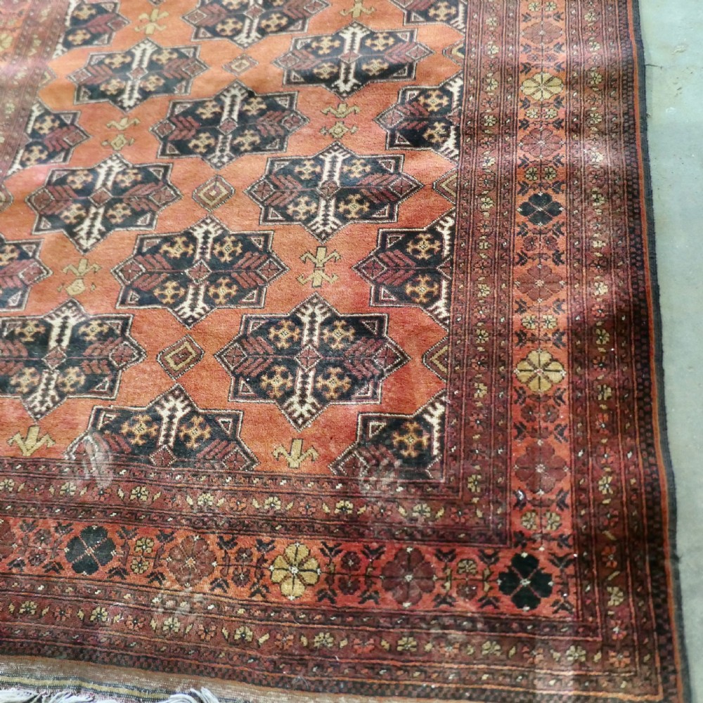 A rectangular vintage wool area rug featuring dark brown and navy geometric motifs on a terracotta red field with patterned borders and fringe. View III