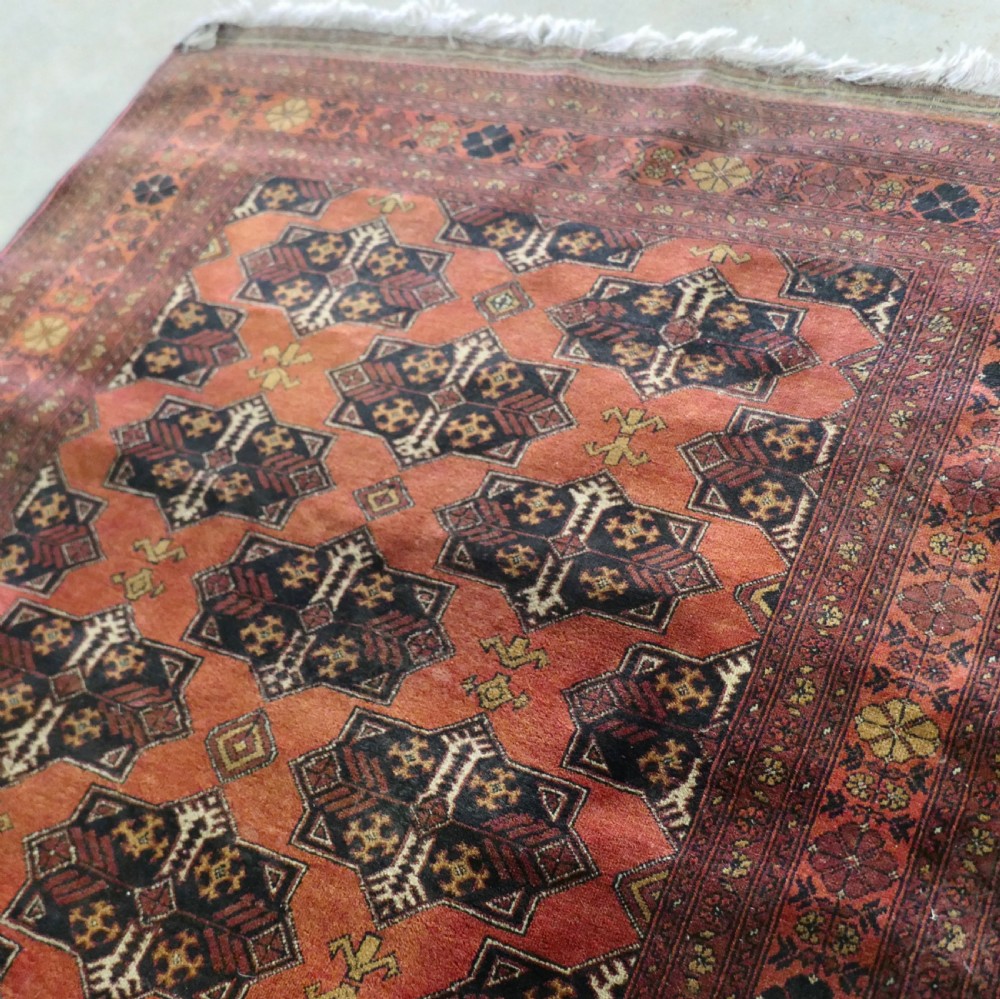 A rectangular vintage wool area rug featuring dark brown and navy geometric motifs on a terracotta red field with patterned borders and fringe. View V