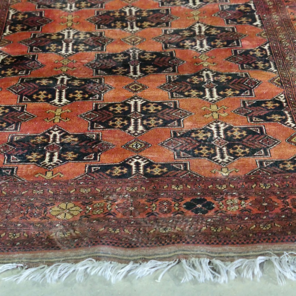 A rectangular vintage wool area rug featuring dark brown and navy geometric motifs on a terracotta red field with patterned borders and fringe. View VII