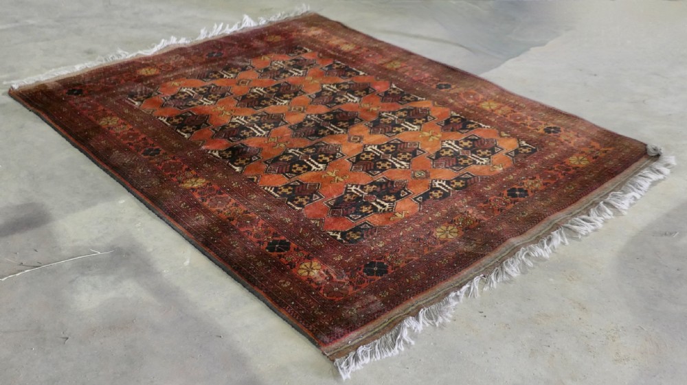 A rectangular vintage wool area rug featuring dark brown and navy geometric motifs on a terracotta red field with patterned borders and fringe. View VIII