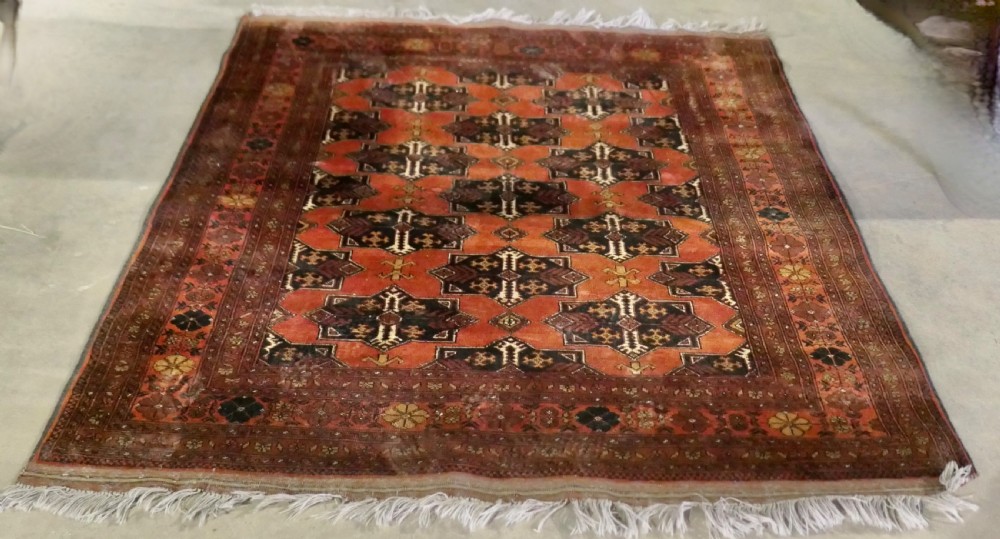 A rectangular vintage wool area rug featuring dark brown and navy geometric motifs on a terracotta red field with patterned borders and fringe. View IX