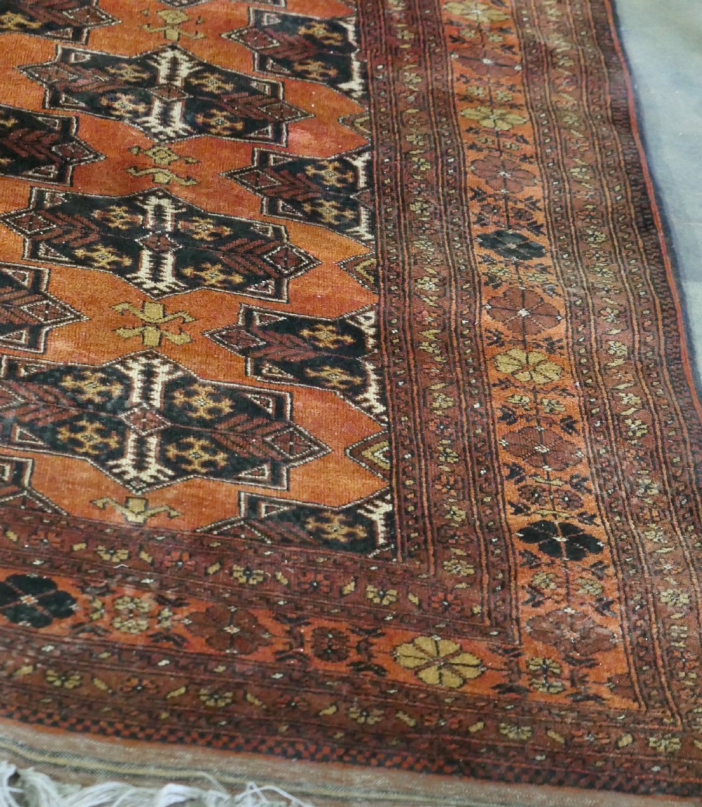 A rectangular vintage wool area rug featuring dark brown and navy geometric motifs on a terracotta red field with patterned borders and fringe. View XI