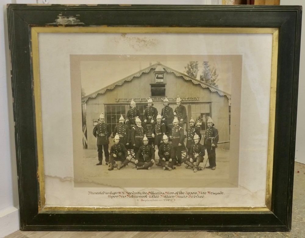 A large Edwardian framed photograph showing a posed group of firefighters in uniform in front of a fire station with a calligraphic inscription along the bottom. View II