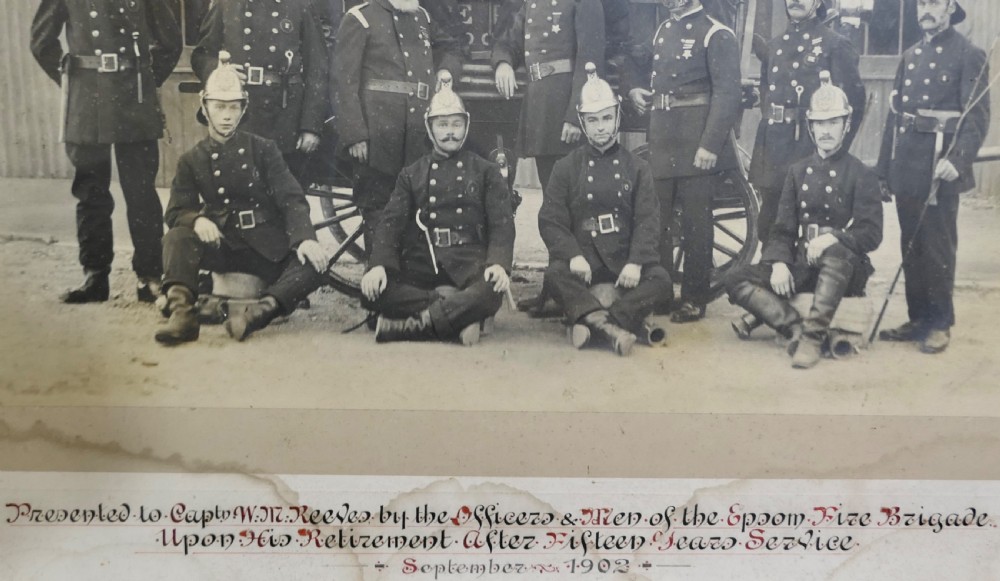 A large Edwardian framed photograph showing a posed group of firefighters in uniform in front of a fire station with a calligraphic inscription along the bottom. View V