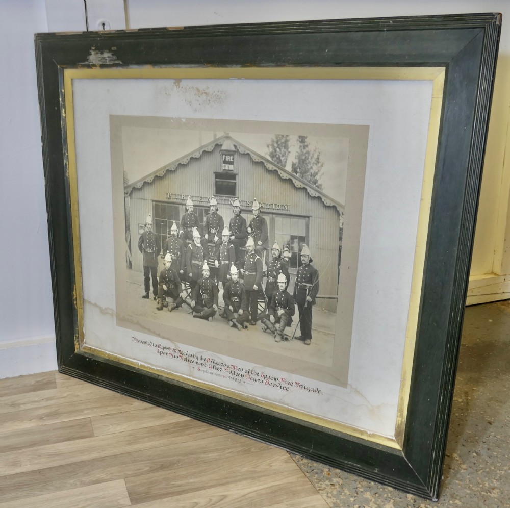 A large Edwardian framed photograph showing a posed group of firefighters in uniform in front of a fire station with a calligraphic inscription along the bottom. View VI