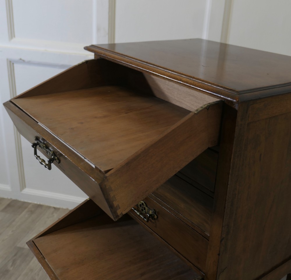 An Arts and Crafts warm brown wood music cabinet with five drawers featuring ornamental brass drop handles, raised on tapered legs with castors and a lower shelf. View IX