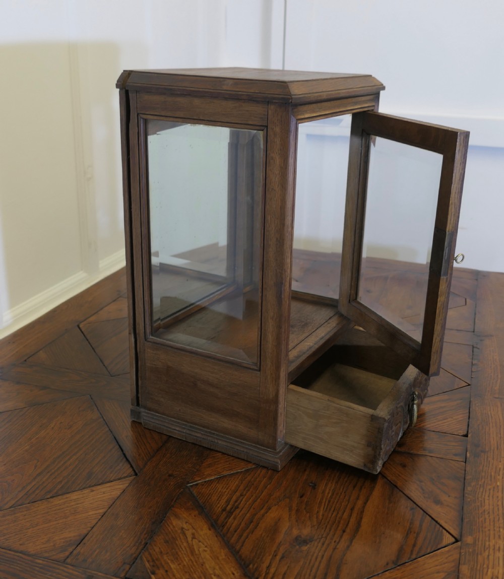 An antique oak countertop display cabinet featuring a glass-panelled door, mirrored interior back, and a lower drawer decorated with hand-carved relief patterns. View VII