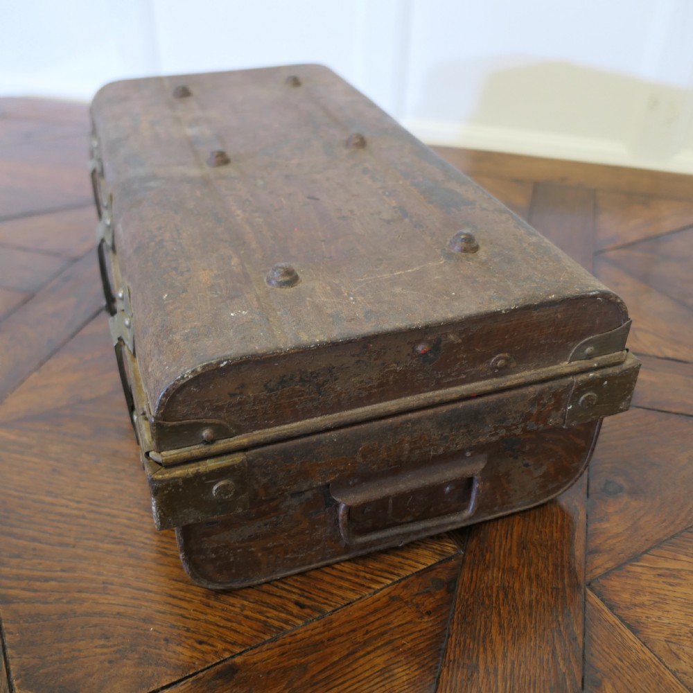 A small dark brown steel cabin trunk featuring three front metal latches, a central folding handle, and painted lettering reading Best Steel Cabin Trunk. View II