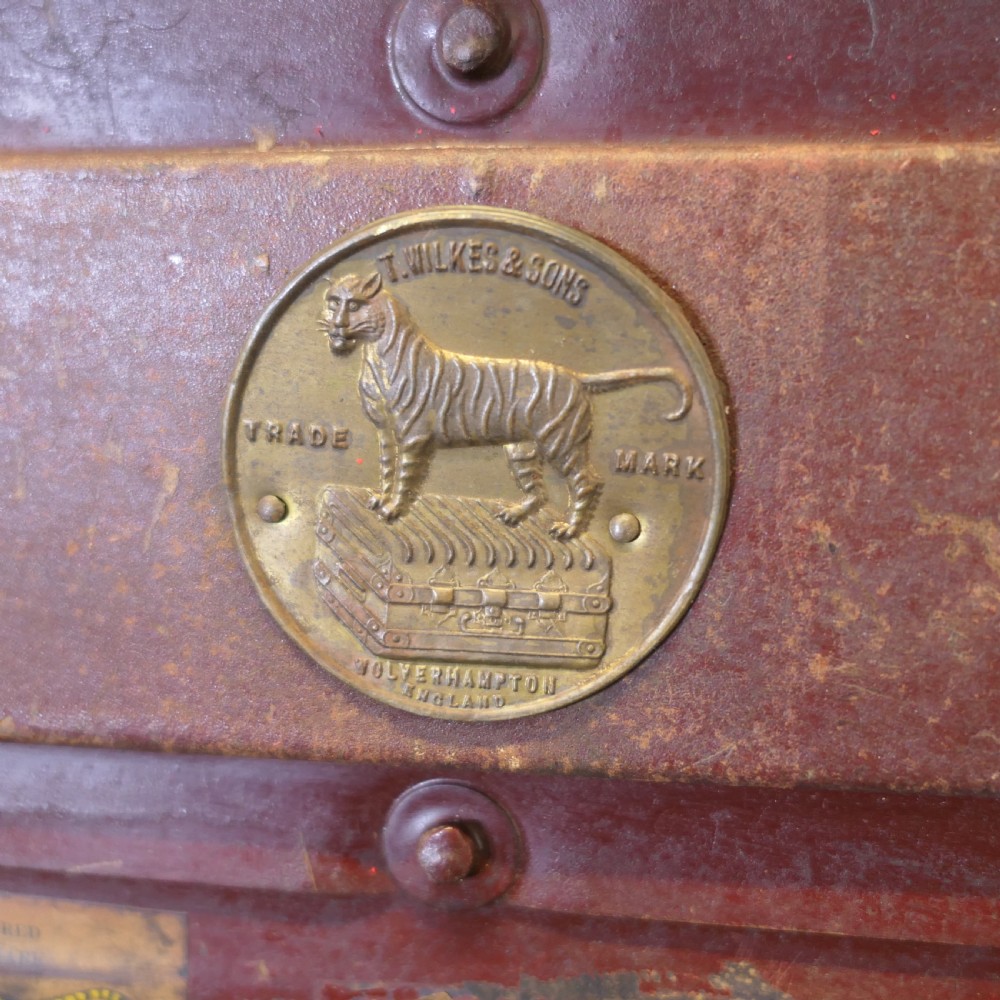 A small dark brown steel cabin trunk featuring three front metal latches, a central folding handle, and painted lettering reading Best Steel Cabin Trunk. View IV