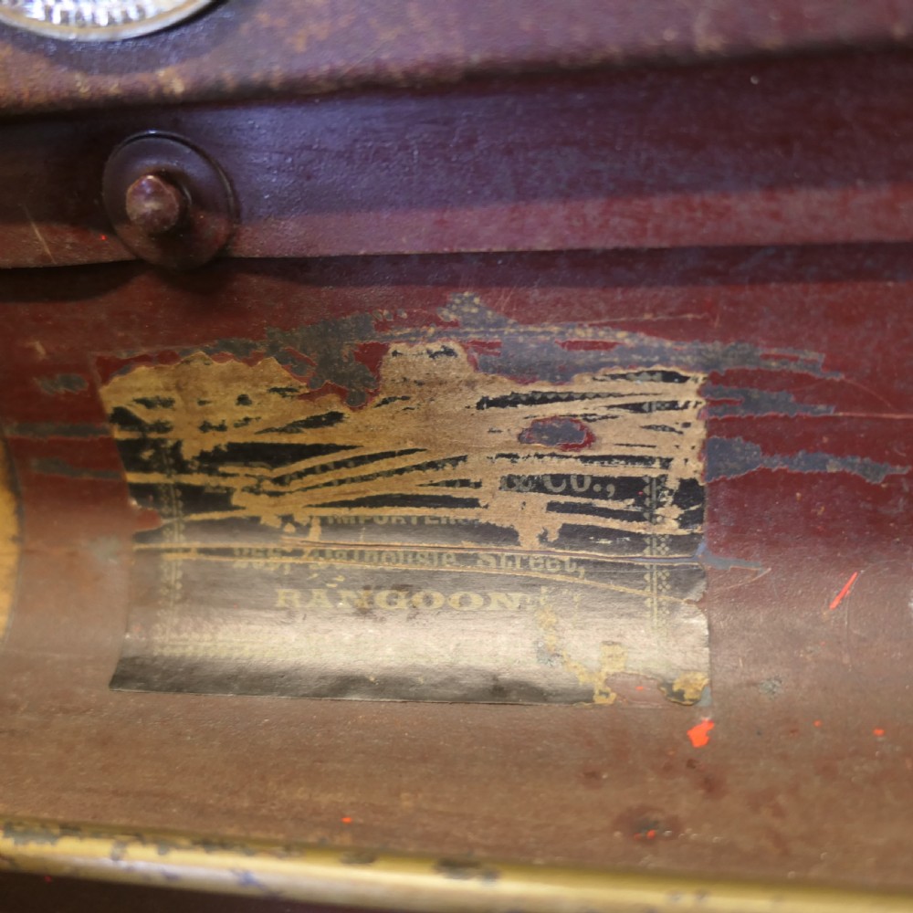 A small dark brown steel cabin trunk featuring three front metal latches, a central folding handle, and painted lettering reading Best Steel Cabin Trunk. View VI