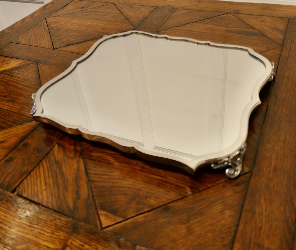 A French Art Deco silver-plated tray featuring a shaped mirror base with scalloped edges and cast scroll feet.