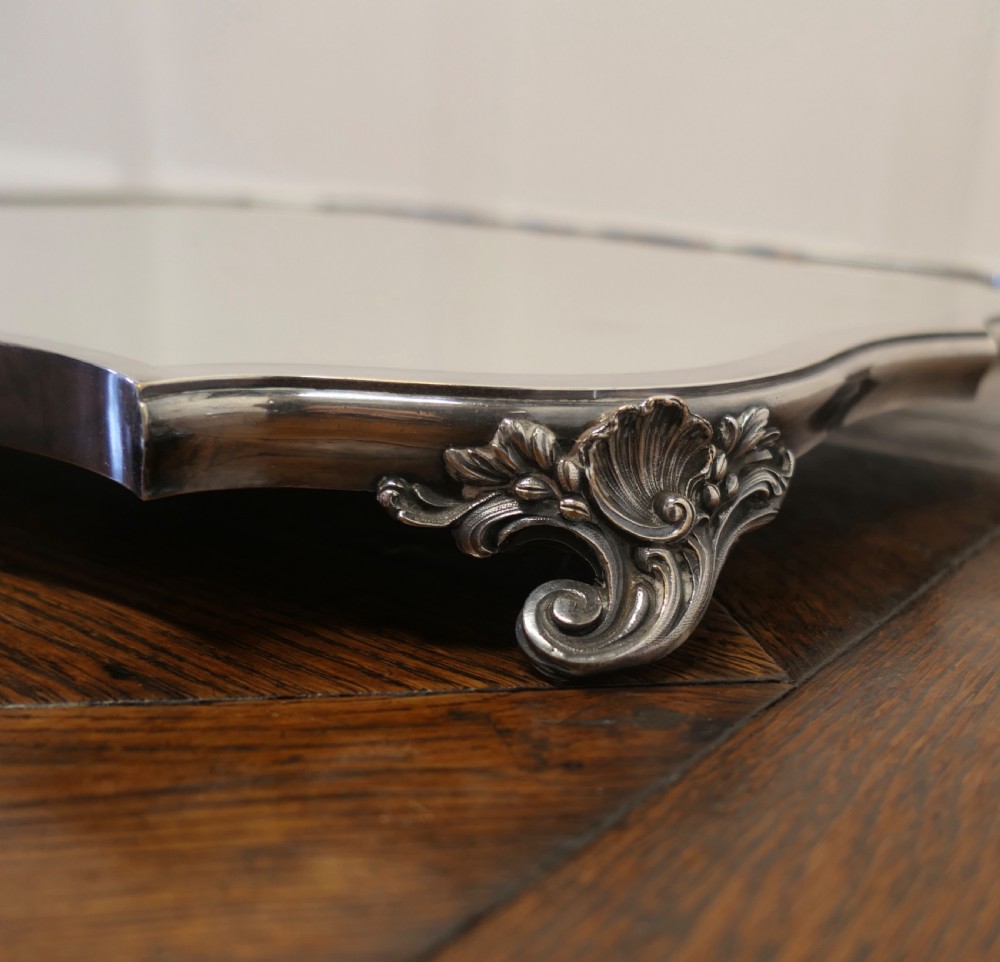 A French Art Deco silver-plated tray featuring a shaped mirror base with scalloped edges and cast scroll feet. View II