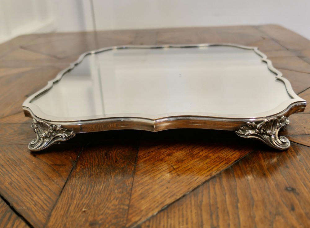 A French Art Deco silver-plated tray featuring a shaped mirror base with scalloped edges and cast scroll feet. View III