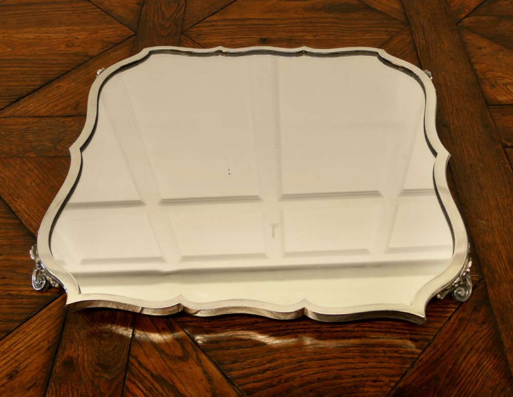 A French Art Deco silver-plated tray featuring a shaped mirror base with scalloped edges and cast scroll feet. View IV