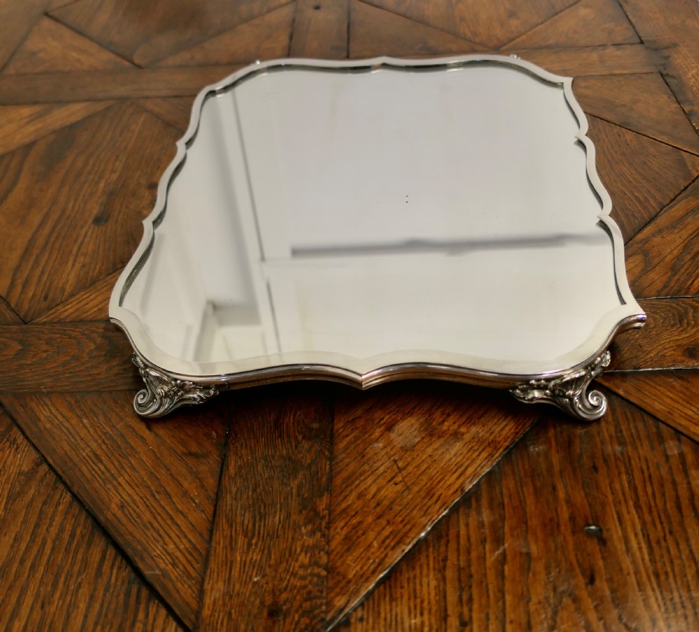 A French Art Deco silver-plated tray featuring a shaped mirror base with scalloped edges and cast scroll feet. View VI