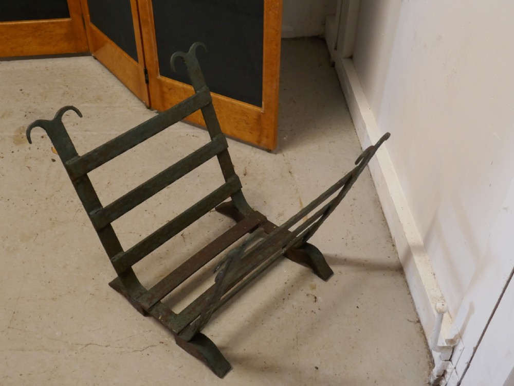 A heavy hand-forged wrought iron log carrier with angled side slats, scrolled finials, and a patinated green and rust finish. View III