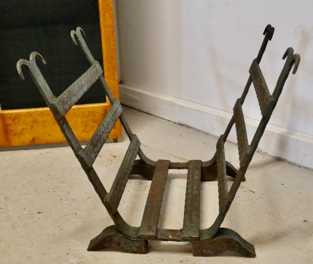 A heavy hand-forged wrought iron log carrier with angled side slats, scrolled finials, and a patinated green and rust finish. View IV