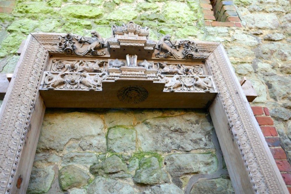 An intricately carved natural teak wooden archway featuring relief carvings of elephants and architectural motifs. View XI