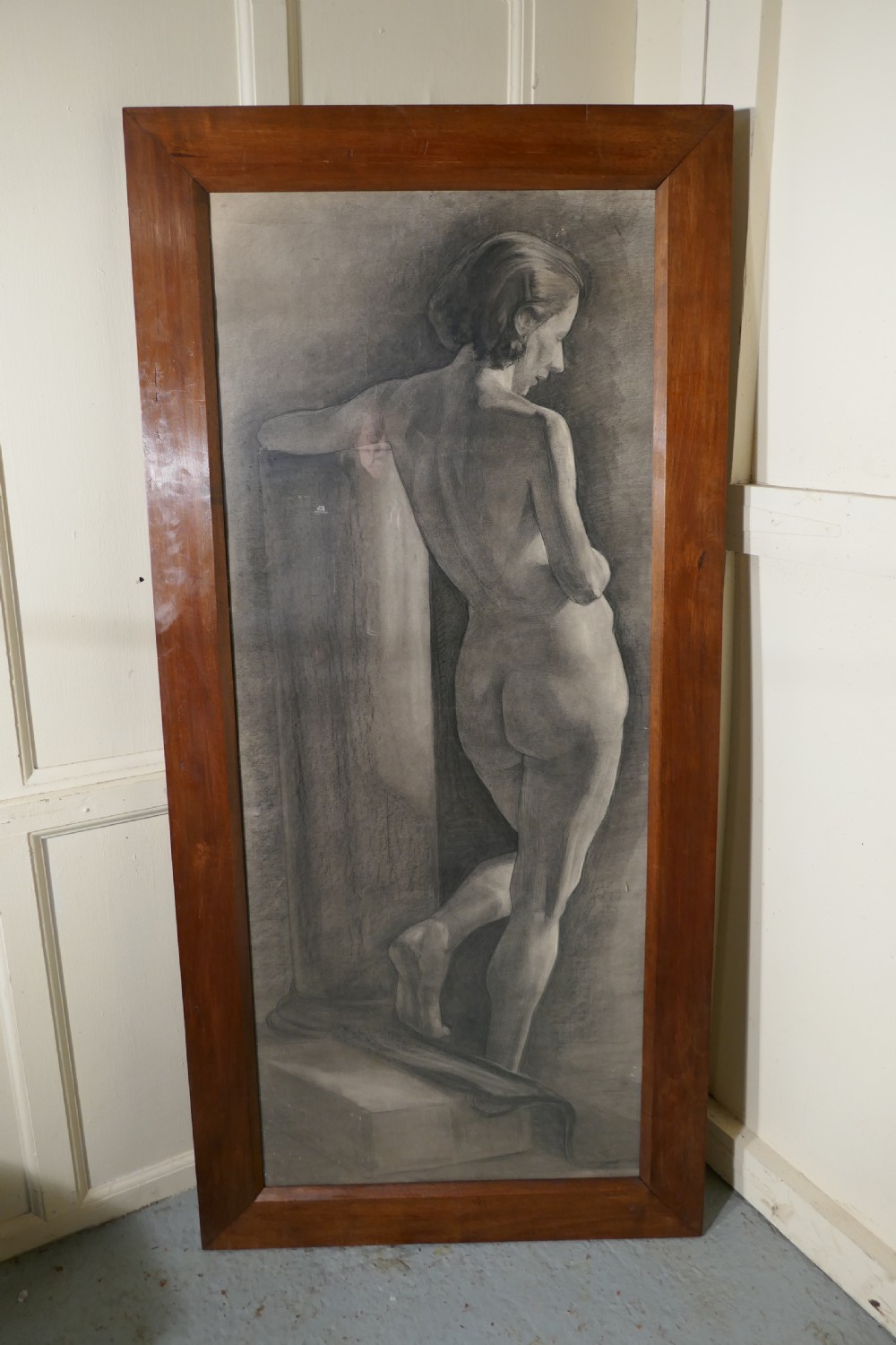 A full-length charcoal study of a standing female nude in profile and back view, set within a polished timber frame.