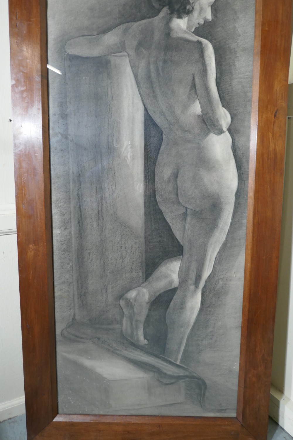A full-length charcoal study of a standing female nude in profile and back view, set within a polished timber frame. View V