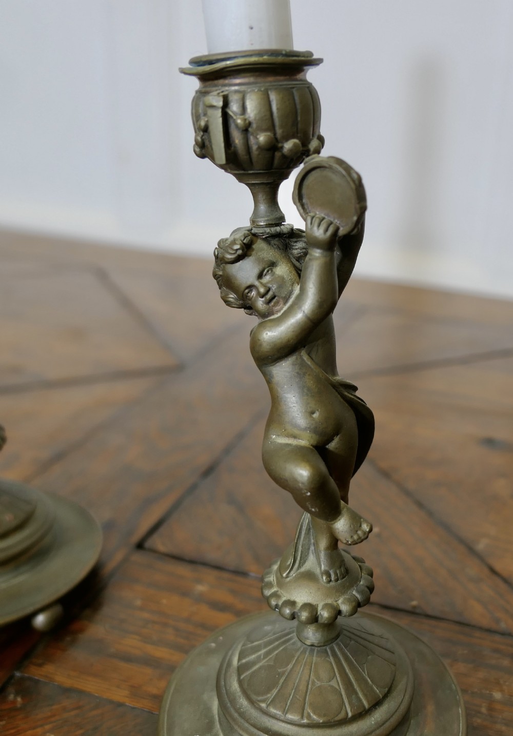 A pair of 19th-century cast brass candlesticks featuring sculpted figures of dancing cherubs supporting fluted sconces on stepped circular bases. View II