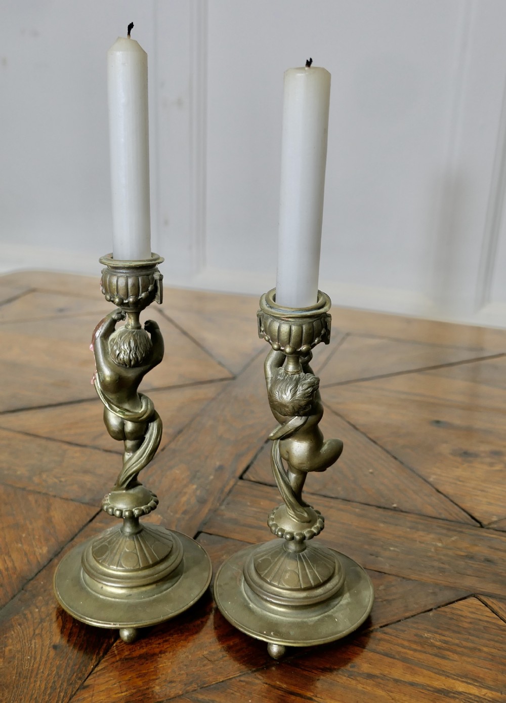 A pair of 19th-century cast brass candlesticks featuring sculpted figures of dancing cherubs supporting fluted sconces on stepped circular bases. View IV