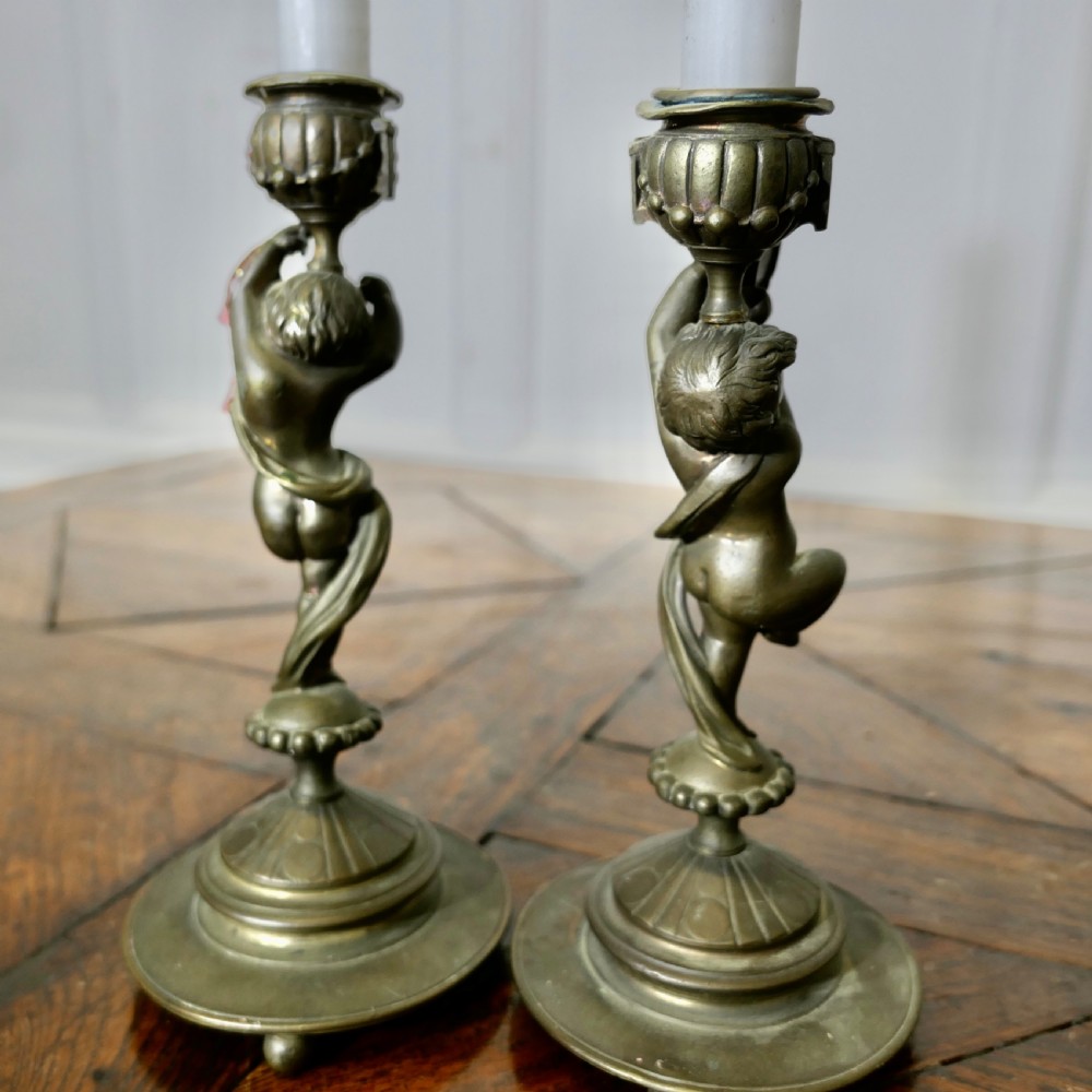 A pair of 19th-century cast brass candlesticks featuring sculpted figures of dancing cherubs supporting fluted sconces on stepped circular bases. View V