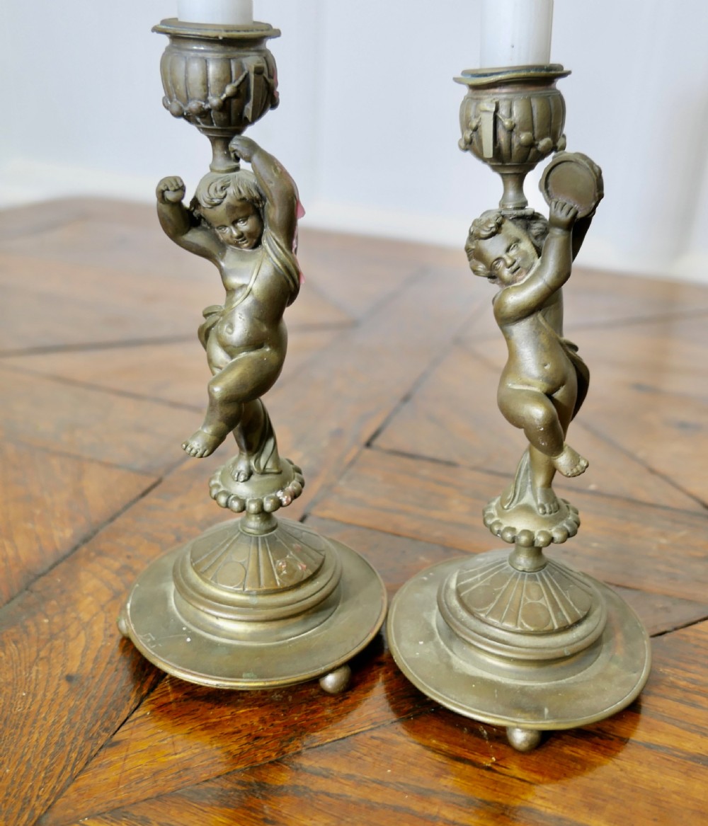 A pair of 19th-century cast brass candlesticks featuring sculpted figures of dancing cherubs supporting fluted sconces on stepped circular bases. View VI