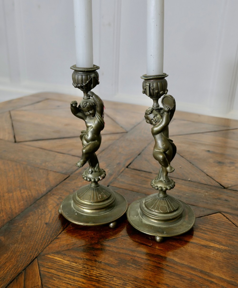 A pair of 19th-century cast brass candlesticks featuring sculpted figures of dancing cherubs supporting fluted sconces on stepped circular bases. View VII