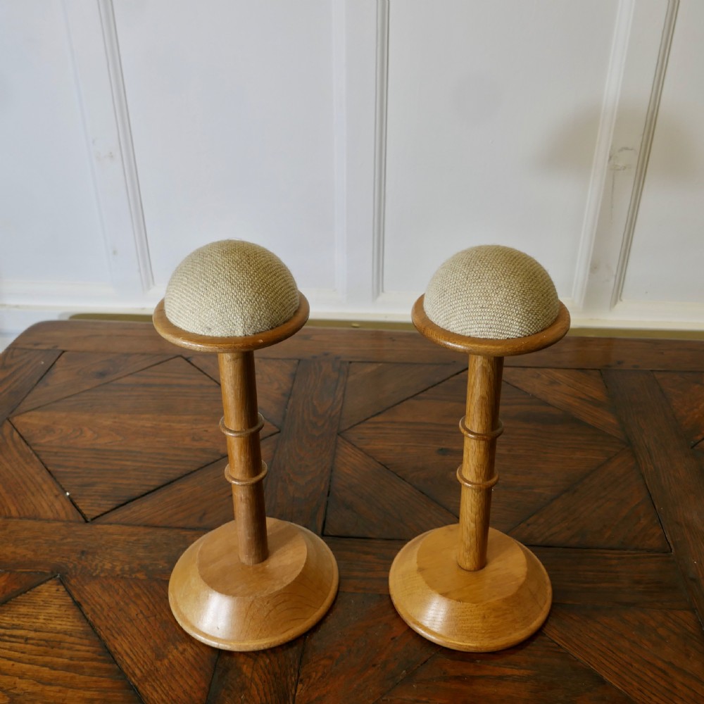 A pair of turned golden oak hat stands featuring circular weighted bases and woven fabric upholstered dome tops. View II