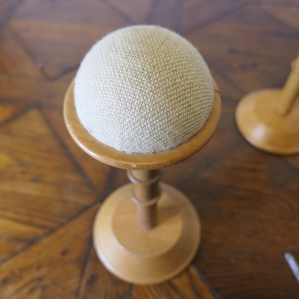 A pair of turned golden oak hat stands featuring circular weighted bases and woven fabric upholstered dome tops. View III