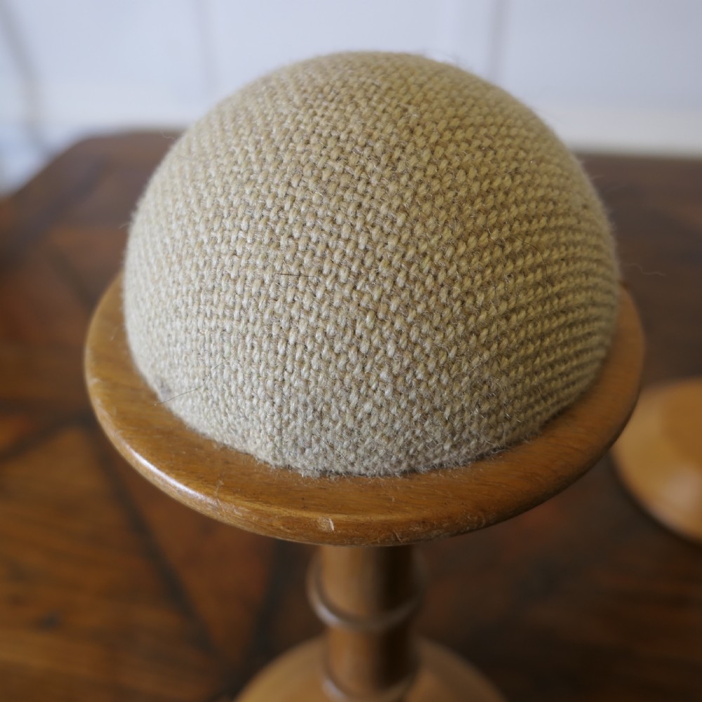 A pair of turned golden oak hat stands featuring circular weighted bases and woven fabric upholstered dome tops. View IV