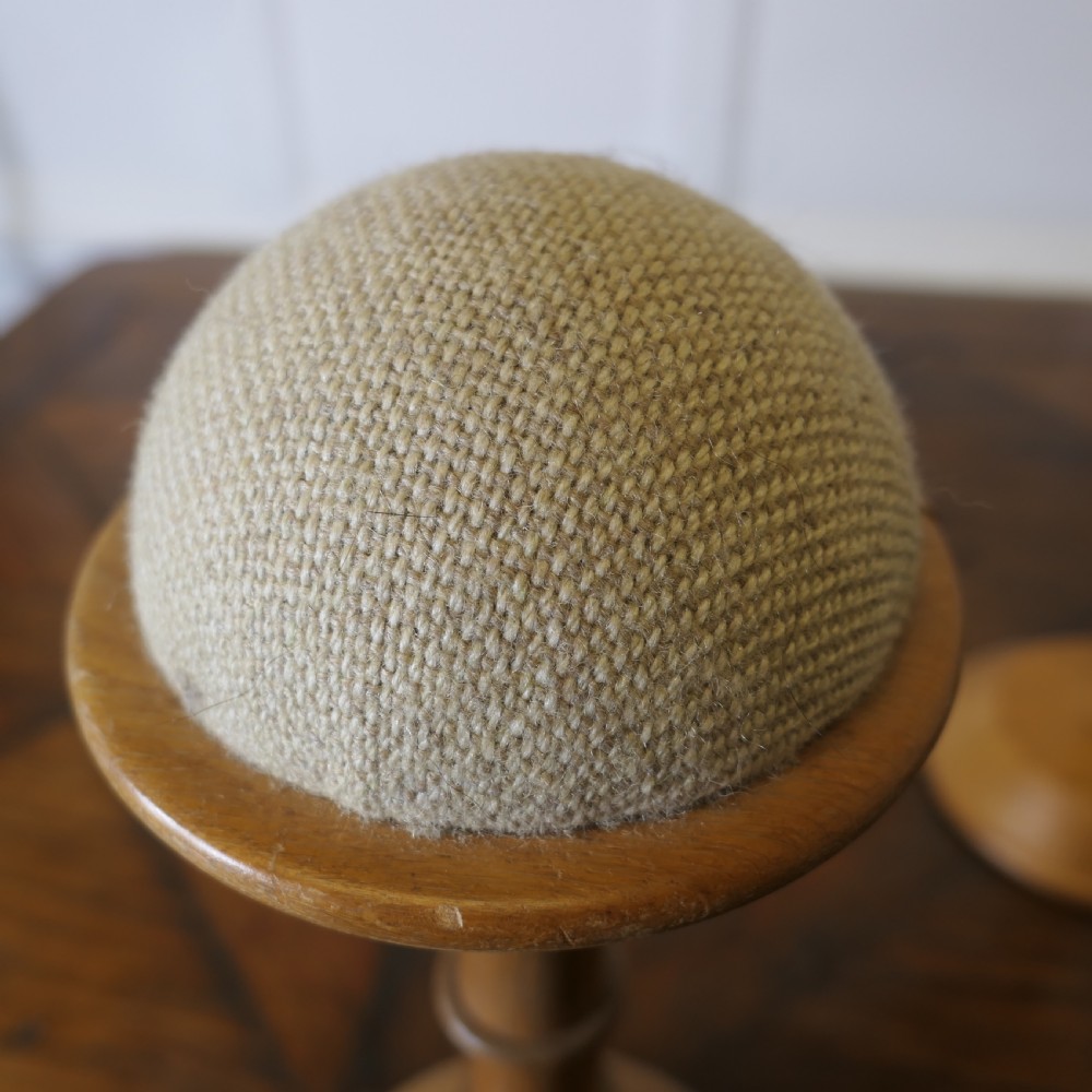 A pair of turned golden oak hat stands featuring circular weighted bases and woven fabric upholstered dome tops. View V