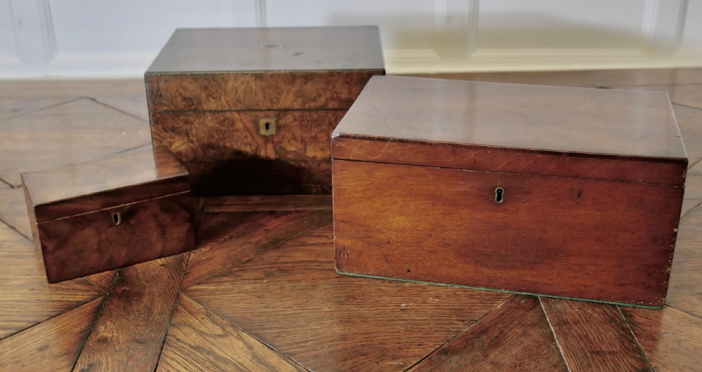 A set of three polished antique burr walnut storage boxes featuring brass keyhole escutcheons resting on a parquet floor.