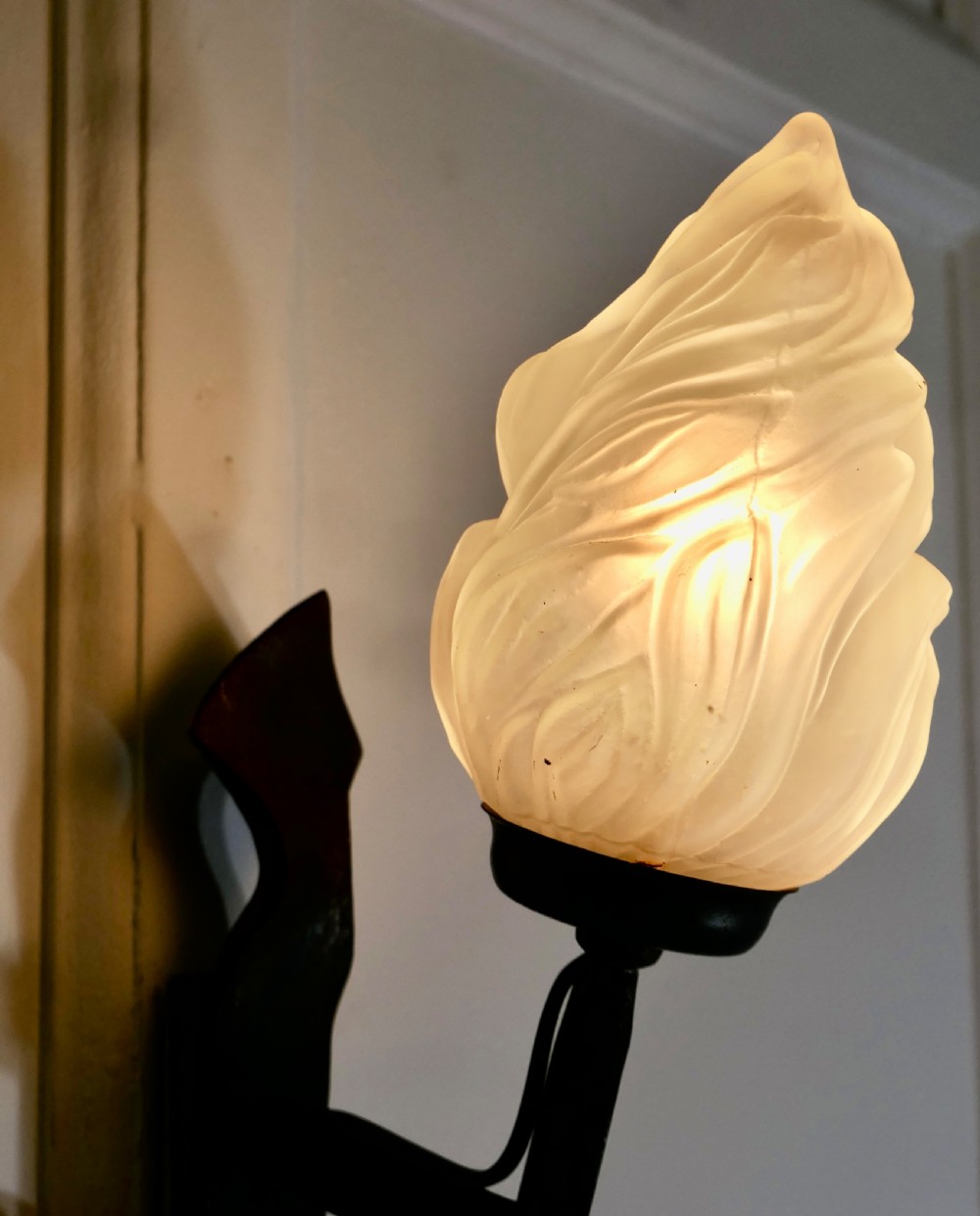 A French Gothic wall sconce made of dark hand-twisted wrought iron holding an illuminated flame-shaped frosted glass shade. View II
