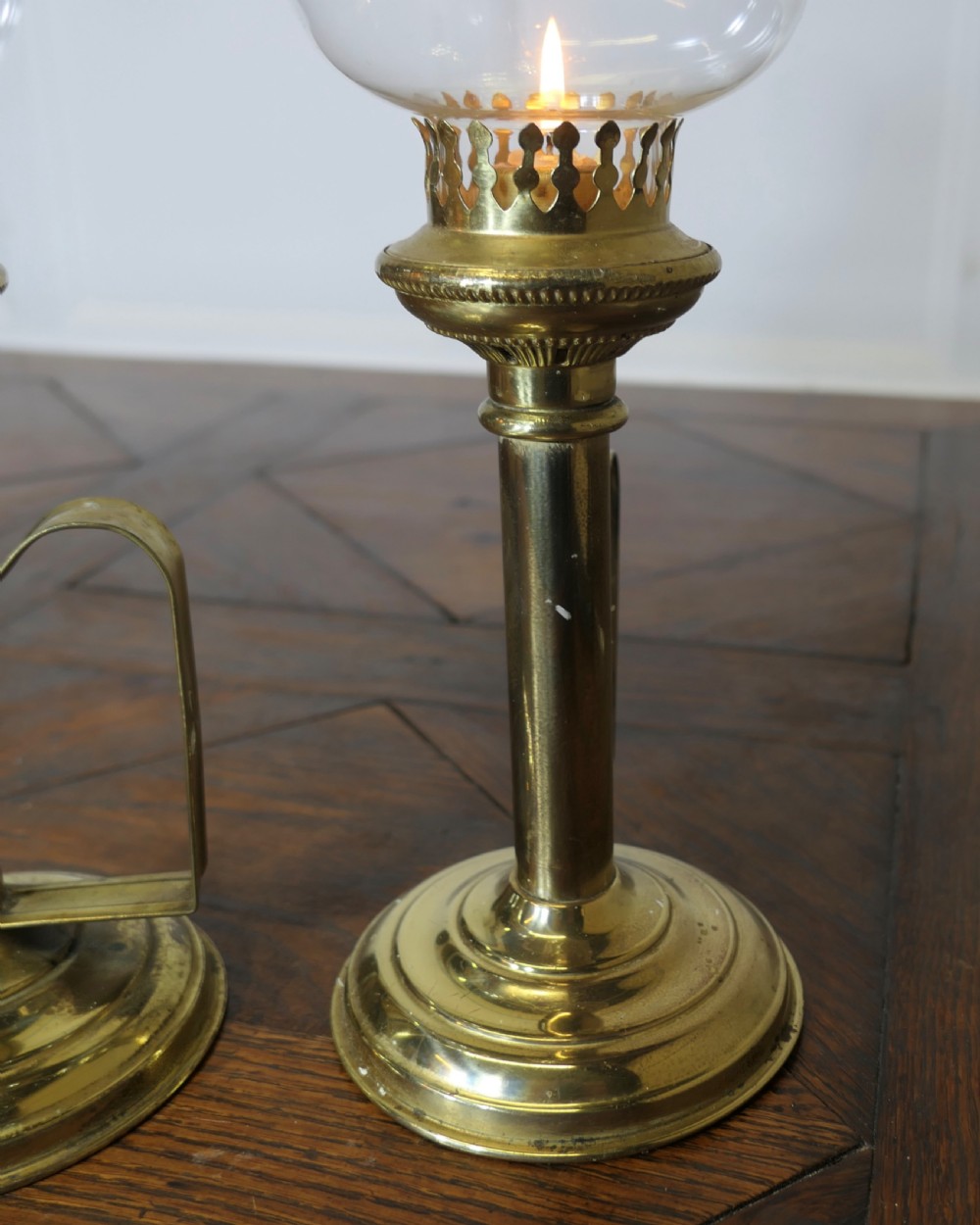 A pair of polished brass candlesticks featuring side handles and removable clear glass hurricane chimneys enclosing lit candles. View IV