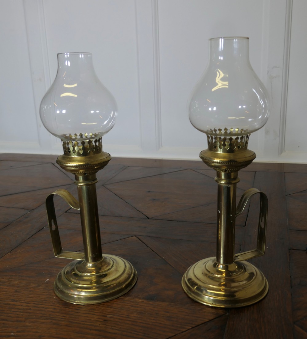 A pair of polished brass candlesticks featuring side handles and removable clear glass hurricane chimneys enclosing lit candles. View VI