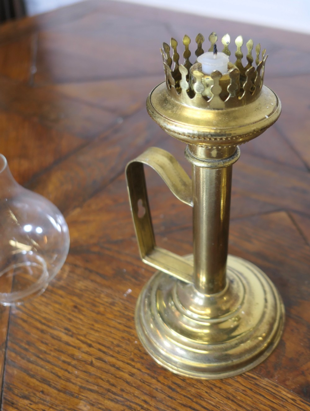 A pair of polished brass candlesticks featuring side handles and removable clear glass hurricane chimneys enclosing lit candles. View IX