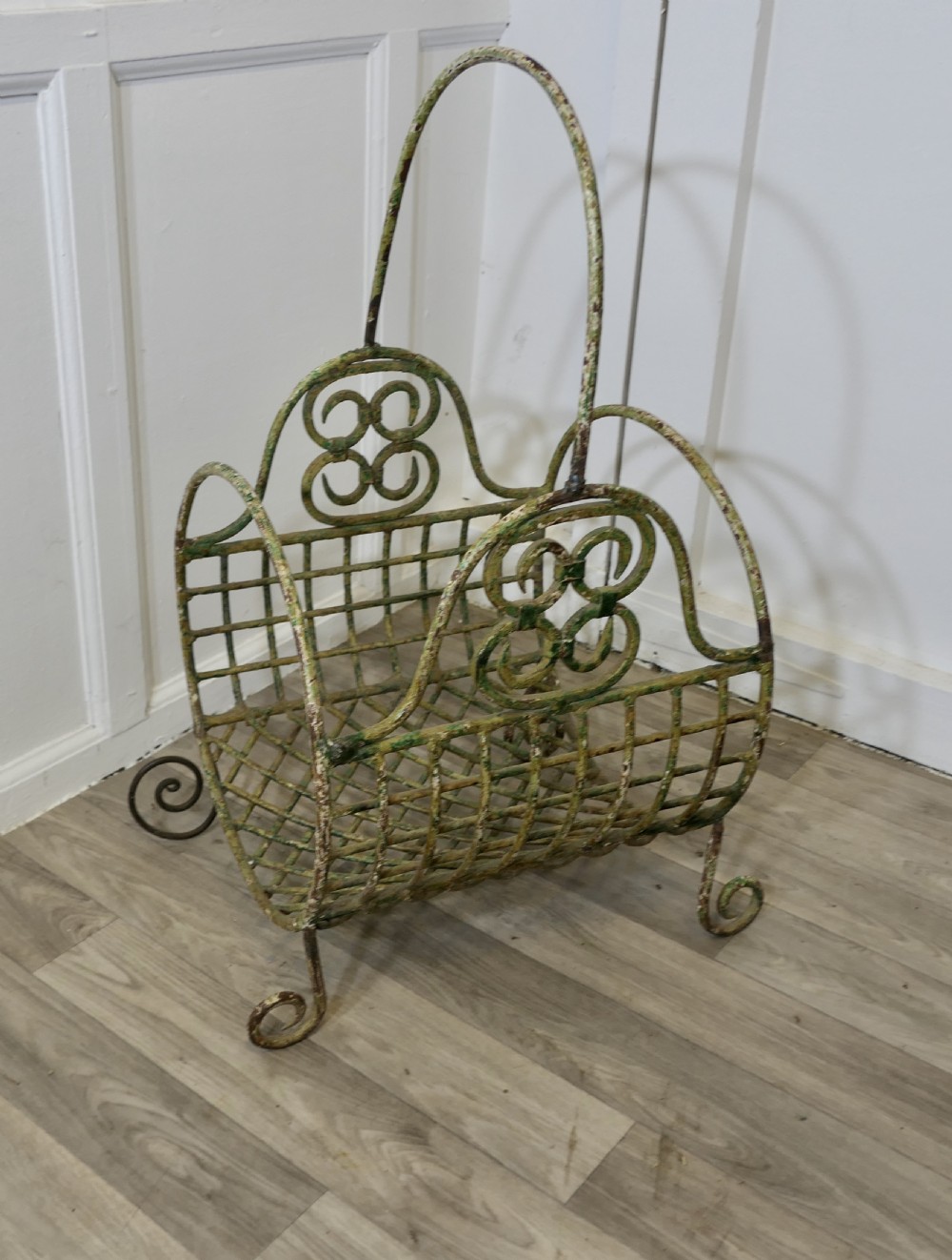A 19th-century French distressed green painted wrought iron wirework log carrier featuring scroll feet, an elevated loop handle, and open mesh grid sides. View IV